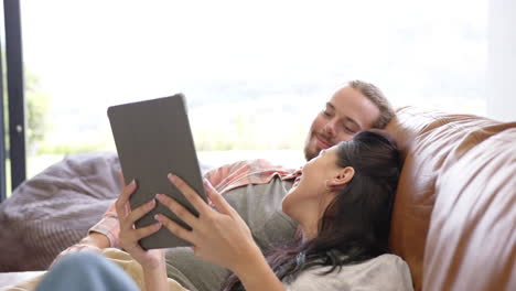 a diverse couple relaxes on a sofa at home, using a tablet