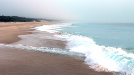 a-beach-with-waves-crashing-on-the-shore-and-bush-on-the-sand-in-the-distance-slow-motion