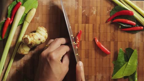 carefully slicing red spicy chili peppers on a bamboo cutting board with a chef knife - top view