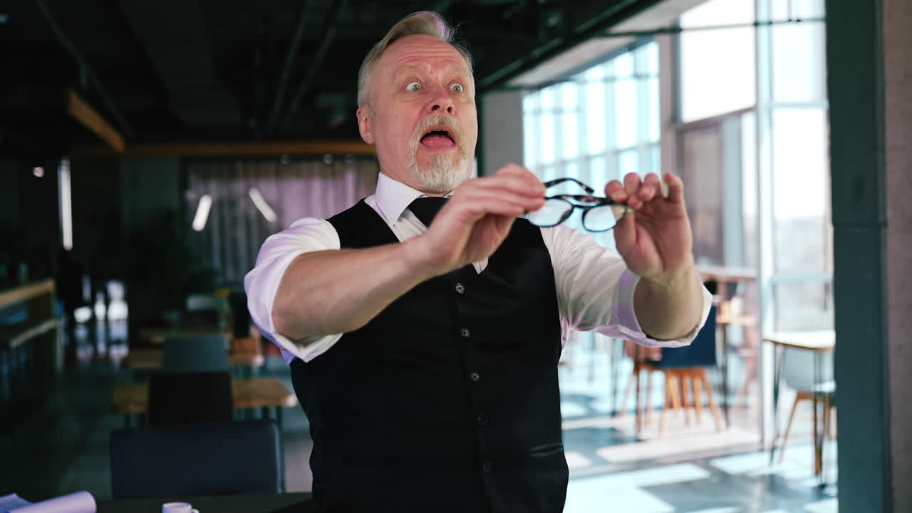 Senior man feeling frustrated and absolutely hopeless without glasses. Male puts on his eyeglasses and looks around with astonishment. Office at backdrop.