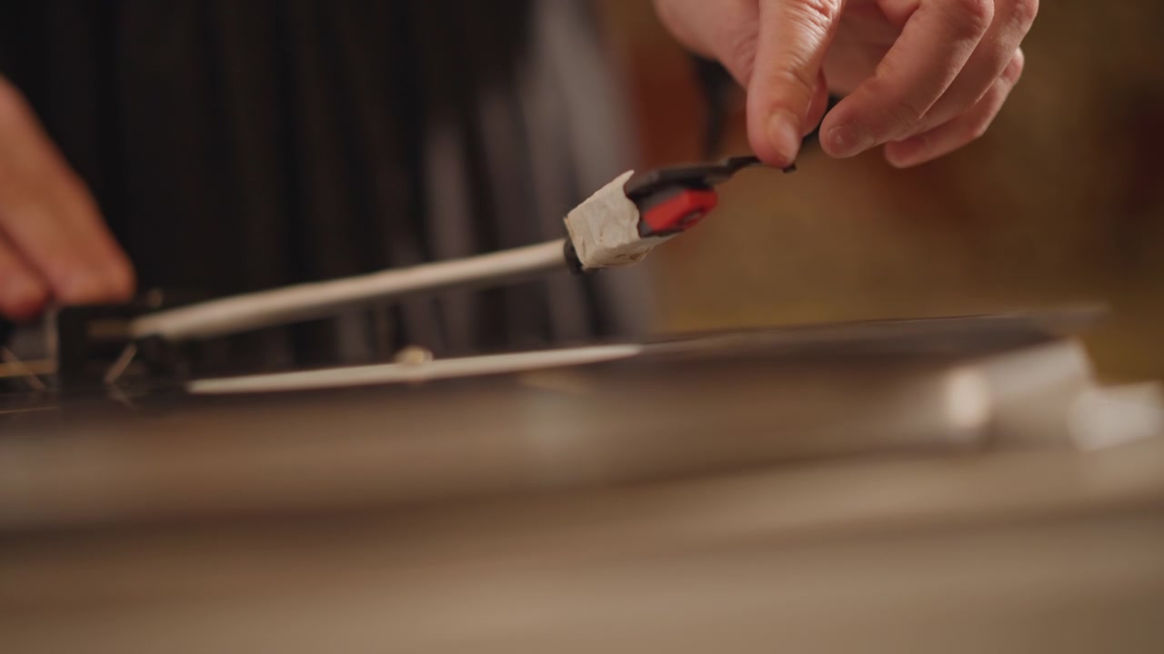 Closeup hand placing stylus on vinyl, warm analog lighting, intimate home audiophile ritual, careful cueing on platter with visible grooves and tactile detail, slow deliberate motion