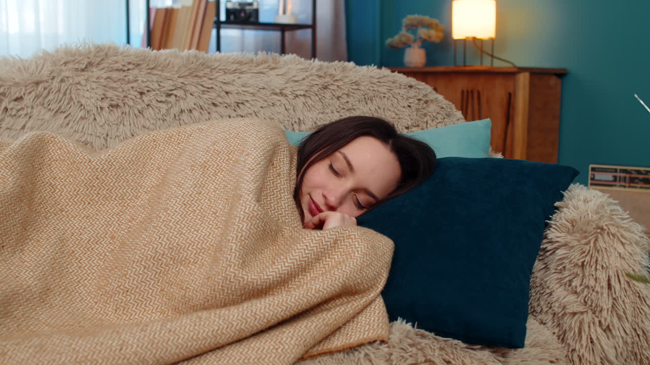 Woman falling asleep tired after exhausting day wrapped in blanket laying head on pillow on sofa