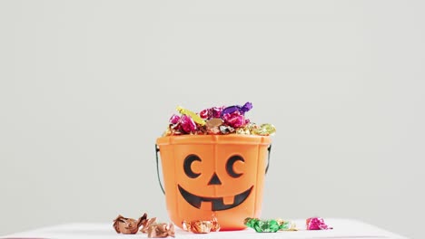 Scary-halloween-pumpkin-printed-bucket-full-of-candies-against-grey-background