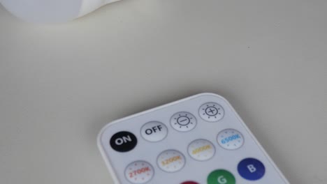smart bulb and remote on neutral background, symbolizing modern tech