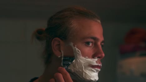 slow motion shot of man shaving his beard with shaving foam and a razor