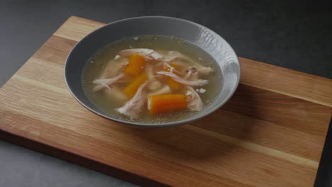 sirviendo sopa de caldo de pollo paleo fresca, caliente y saludable a una tabla de madera sobre fondo de hormigón