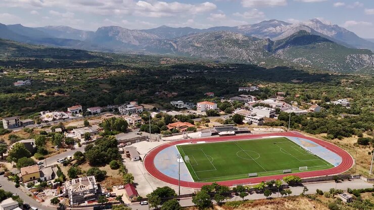 Aerial view of Sardegna football field under sunny skies surrounded by mountains