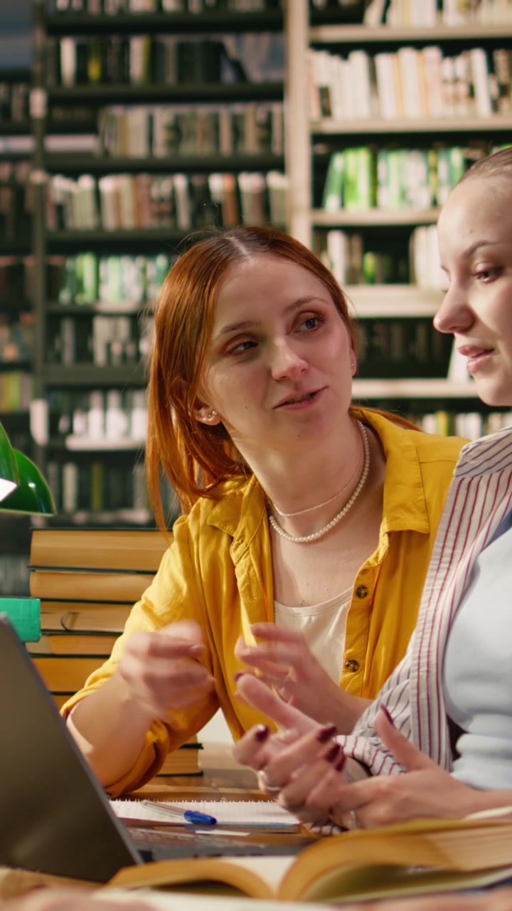 Vertikal video: Mentor veileder student gjennom akademisk arbeid på bærbar PC ved bibliotekbord