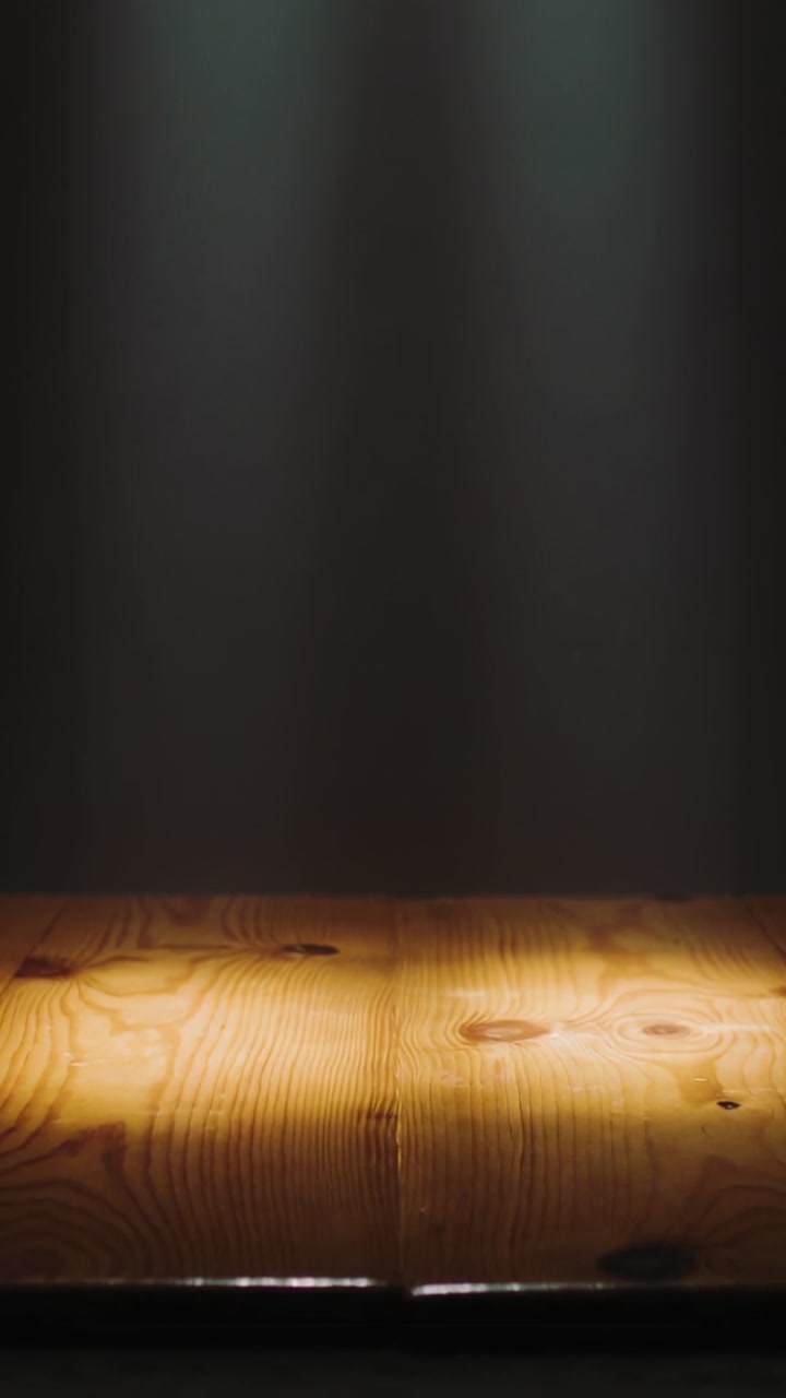 Vertical video: Turning spotlight casting warm pool of light on wood table at studio, showing grain