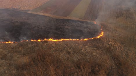 aerial view of spring dry grass burning field. fire and smoke in the meadow, nature pollution, common waste are burned in romania