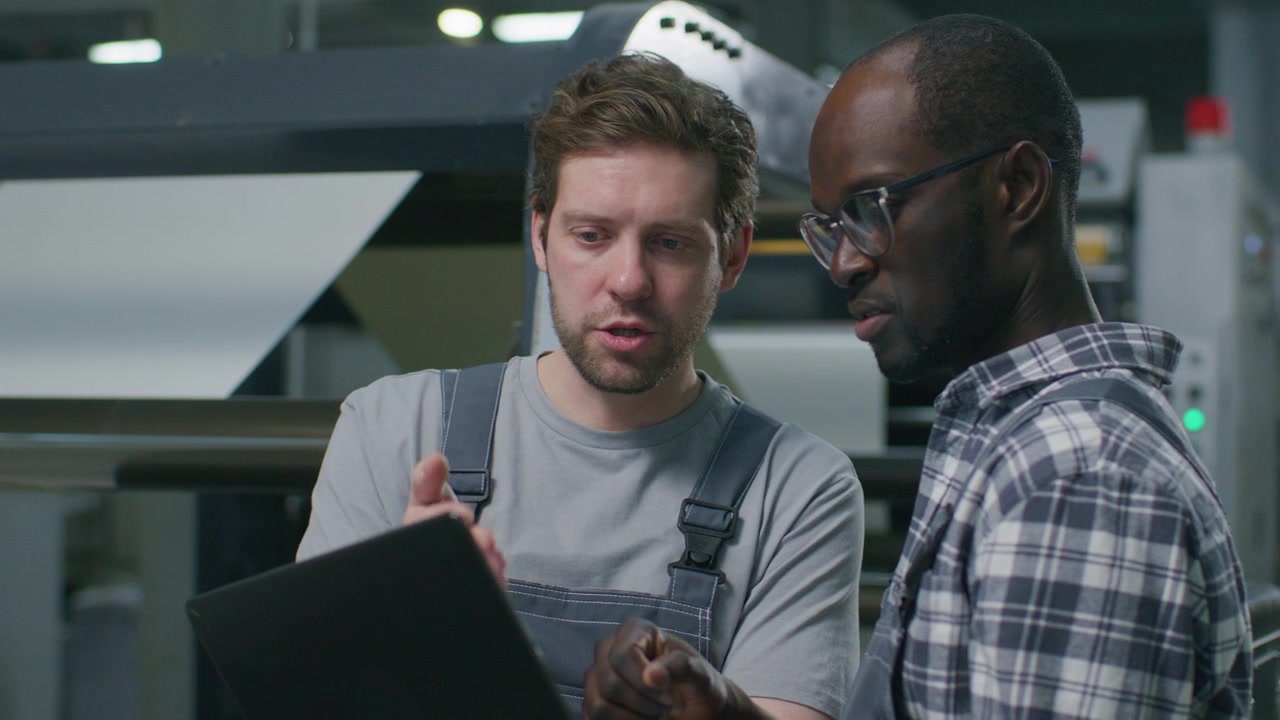 Multiethnic Technicians Using Laptop and Talking in Industrial Print Shop
