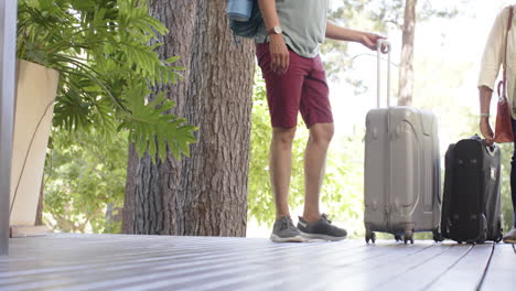 Diverse-senior-couple-walking-with-luggage-to-a-house-in-sunny-outdoors