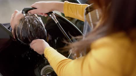 sección media de una peluquera caucásica lavando el cabello de una cliente relajada en una peluquería