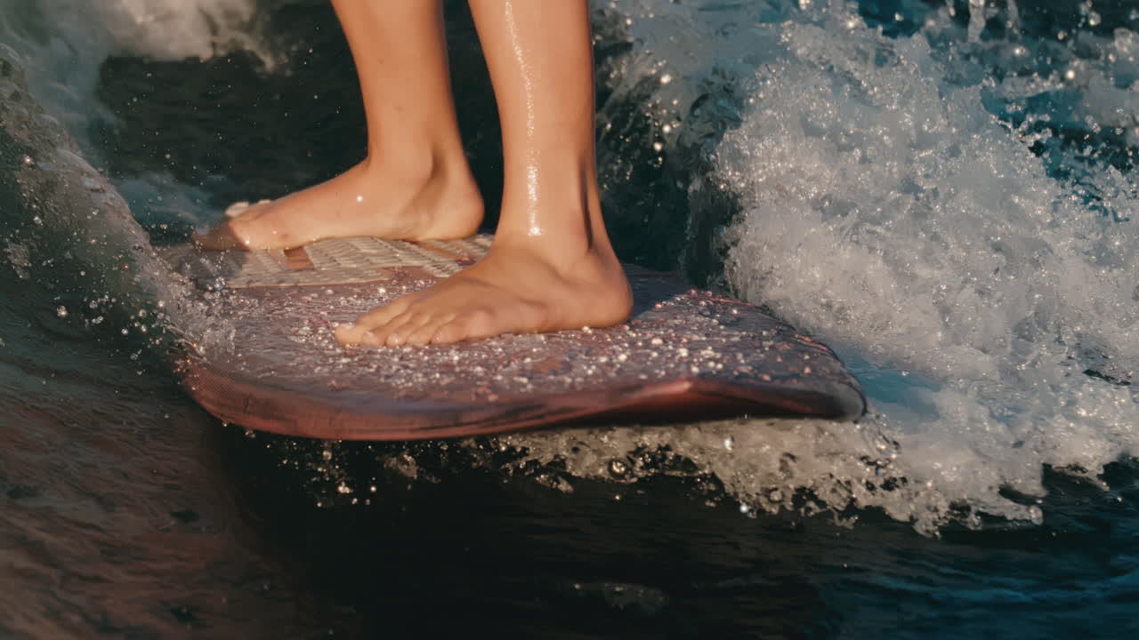 Primo piano dei piedi di una wakeboarder su una tavola rosa che cavalca un'onda perfetta e scintillante sul lago al rallentatore