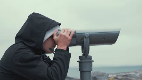 young man looks through sightseeing binoculars bird watching spotting at scenic landscape