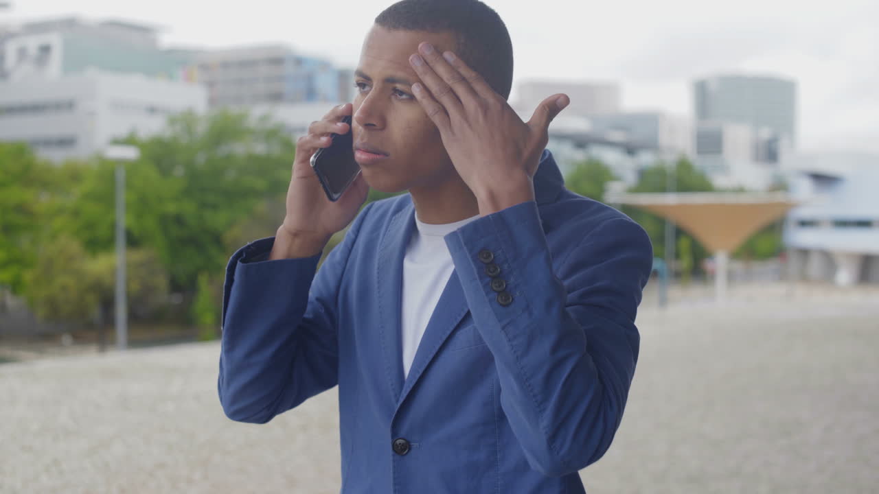 Tired businessman rubbing forehead while talking on phone