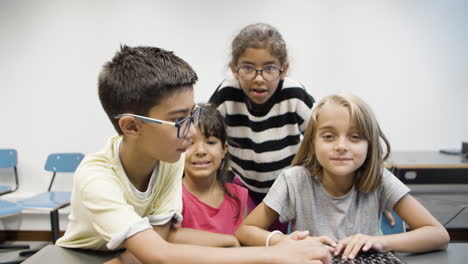 niño y niña escribiendo juntos en el teclado mientras dos compañeros de clase miran el monitor