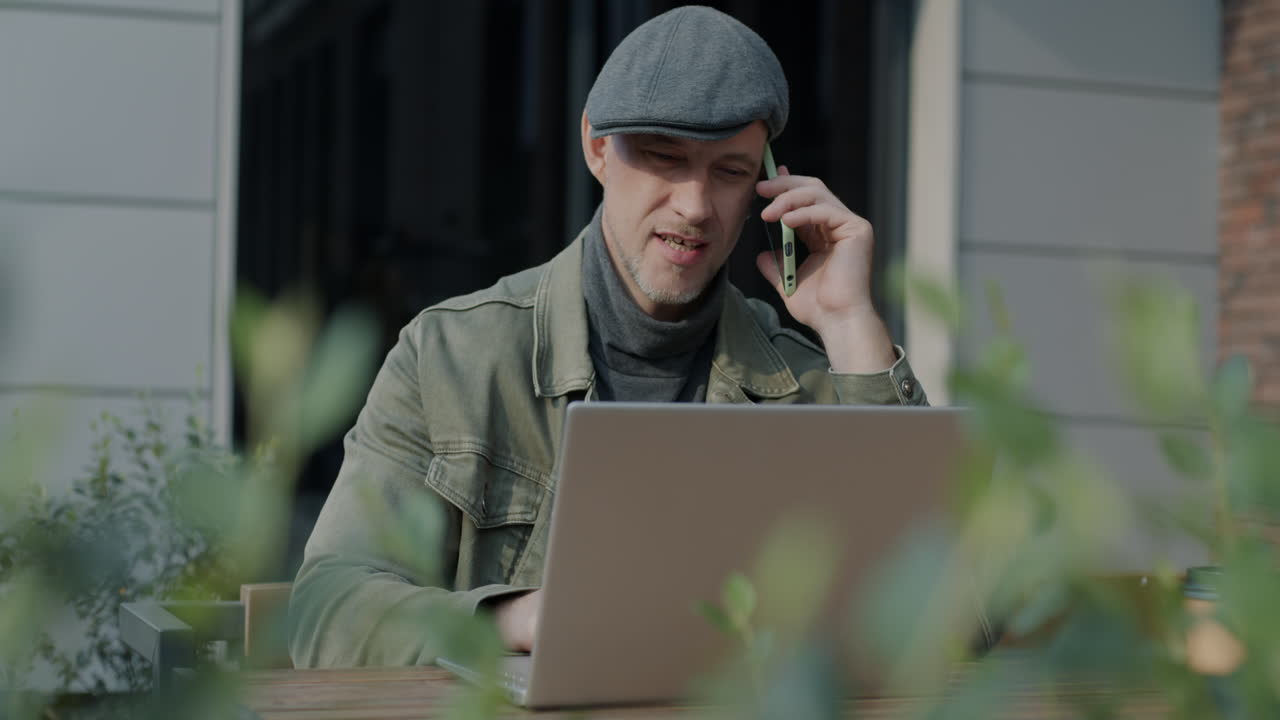 남자가 노트북에서 일하고 야외 카페에서 전화로 이야기하고 있습니다.
