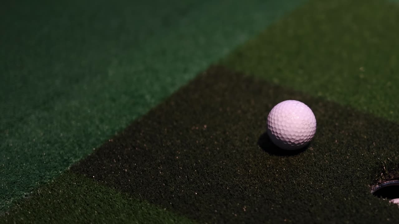 A detailed view of a golf putter striking a ball on a green surface.