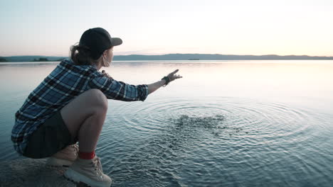 woman sitting by lake and splashing water with hand