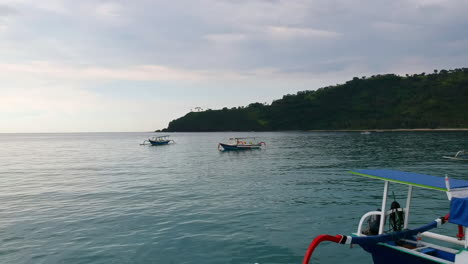 Drone-Shot,-Aerial-view-of-four-wooden-boats-anchored-in-the-water-with-the-island-Lombok-in-the-background