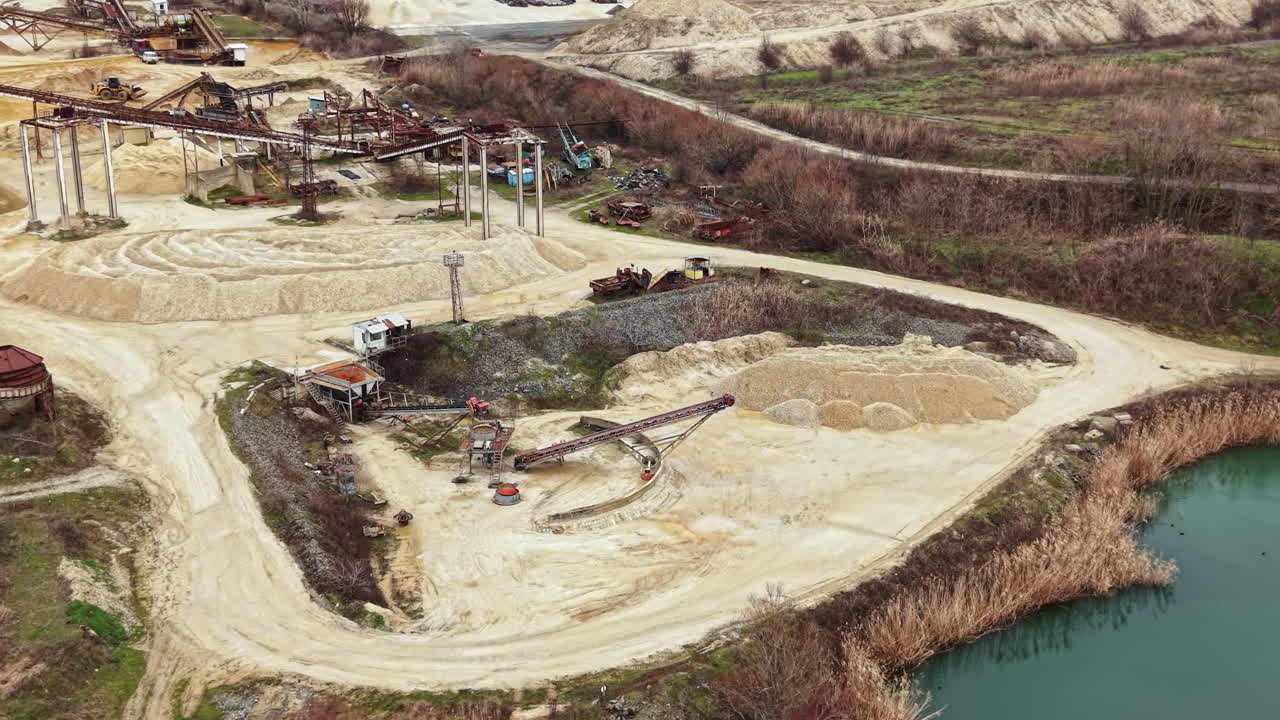 Construction site near water with machinery and stockpiles of materials in a rural area during daytime