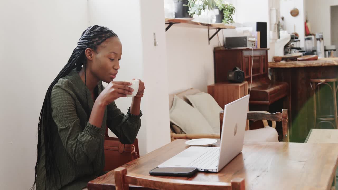 mujer afroamericana feliz usando una computadora portátil y bebiendo café en una cafetería, cámara lenta