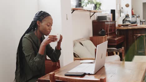 Happy-african-american-woman-using-laptop-and-drinking-coffee-at-coffee-shop,-slow-motion