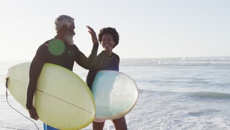 feliz pareja afroamericana caminando con tablas de surf en una playa soleada