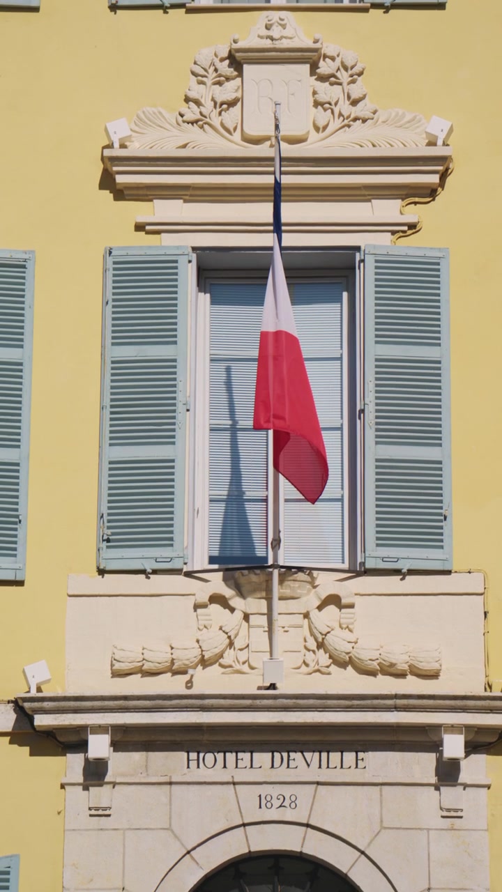 Vista dettagliata dell'Hotel de Ville, con la bandiera francese appesa sopra l'ingresso, persiane blu, elegante decorazione in pietra e l'iscrizione "Hotel de Ville 1828", Antibes, Francia