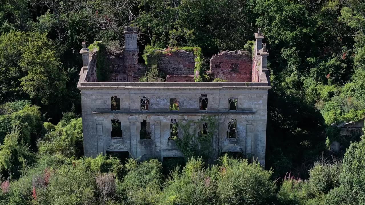 Villa di campagna abbandonata e senza tetto, circondata da alberi incolti, con facciata in pietra fatiscente e pareti interne in mattoni sotto la luminosa luce del sole estivo