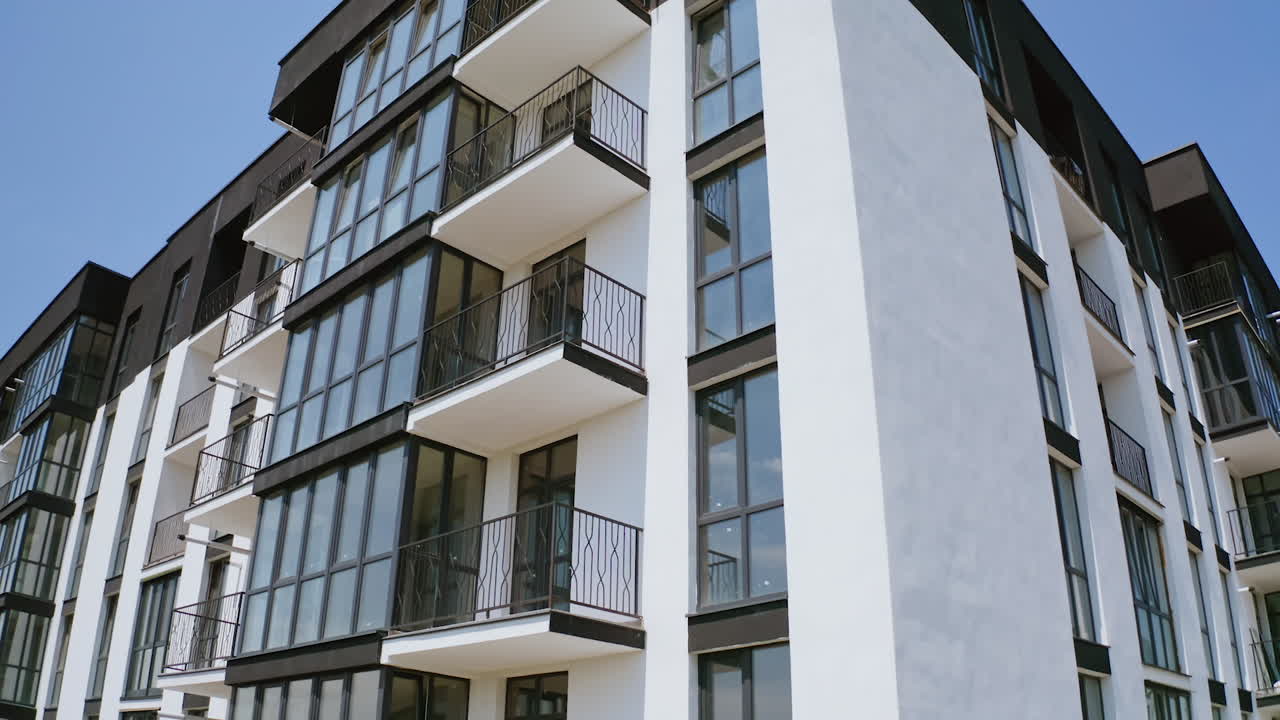 Block of flats on sky background. Modern high-rise apartment building with windows and large balconies. Camera rising up.