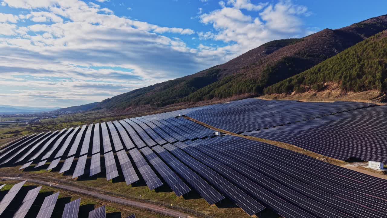 Solpaneler dækker en mark nær en bjergkæde i eftermiddagslys