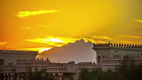 a-castle-behind-which-an-orange-yellow-cloudy-sky-slides-past-the-mountains-and-just-a-little-bit-of-the-sun-can-be-seen-in-it