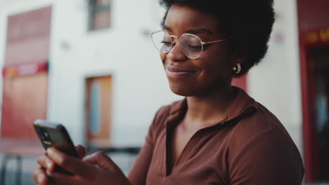 Afrikanisches-Mädchen-Hält-Smartphone-Und-Sieht-Im-Freien-Glücklich-Aus