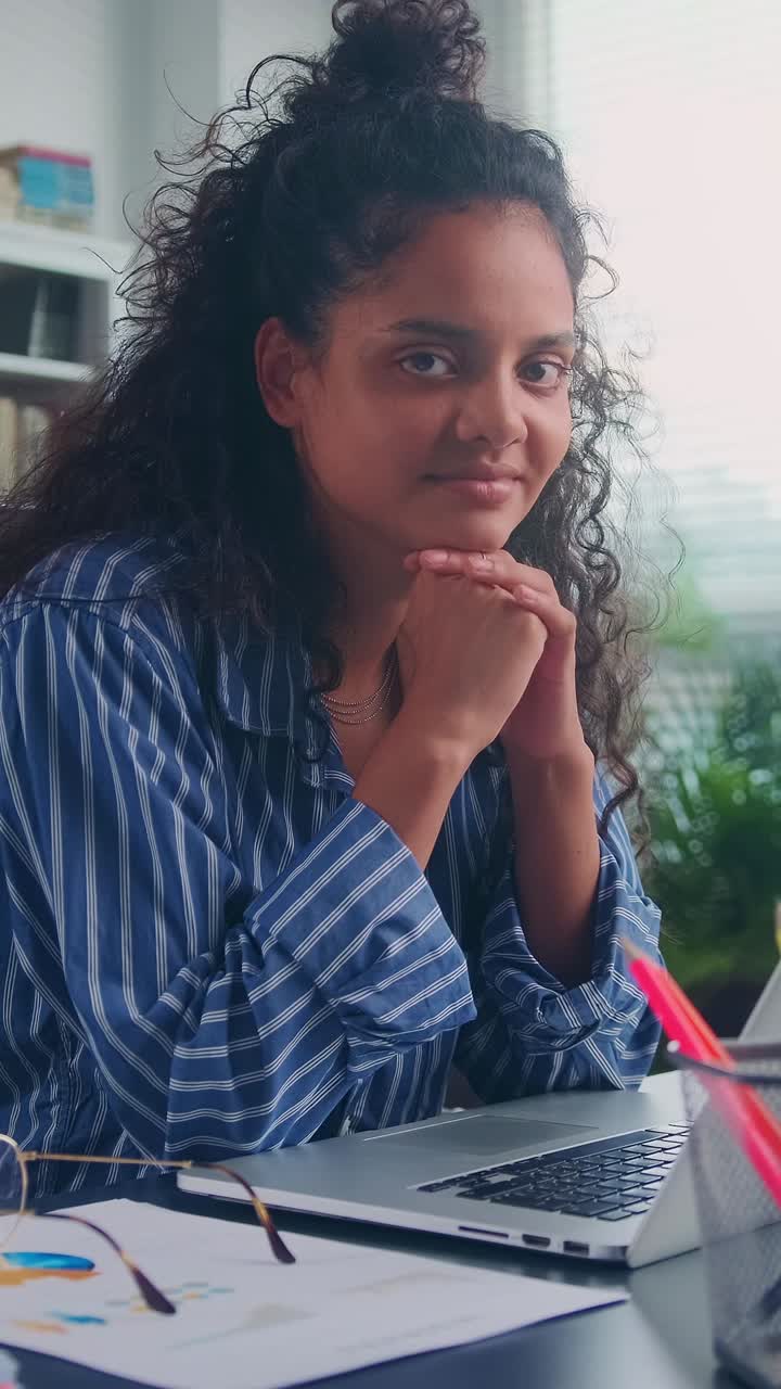 A focused young woman with curly hair sits at a desk in a cozy office