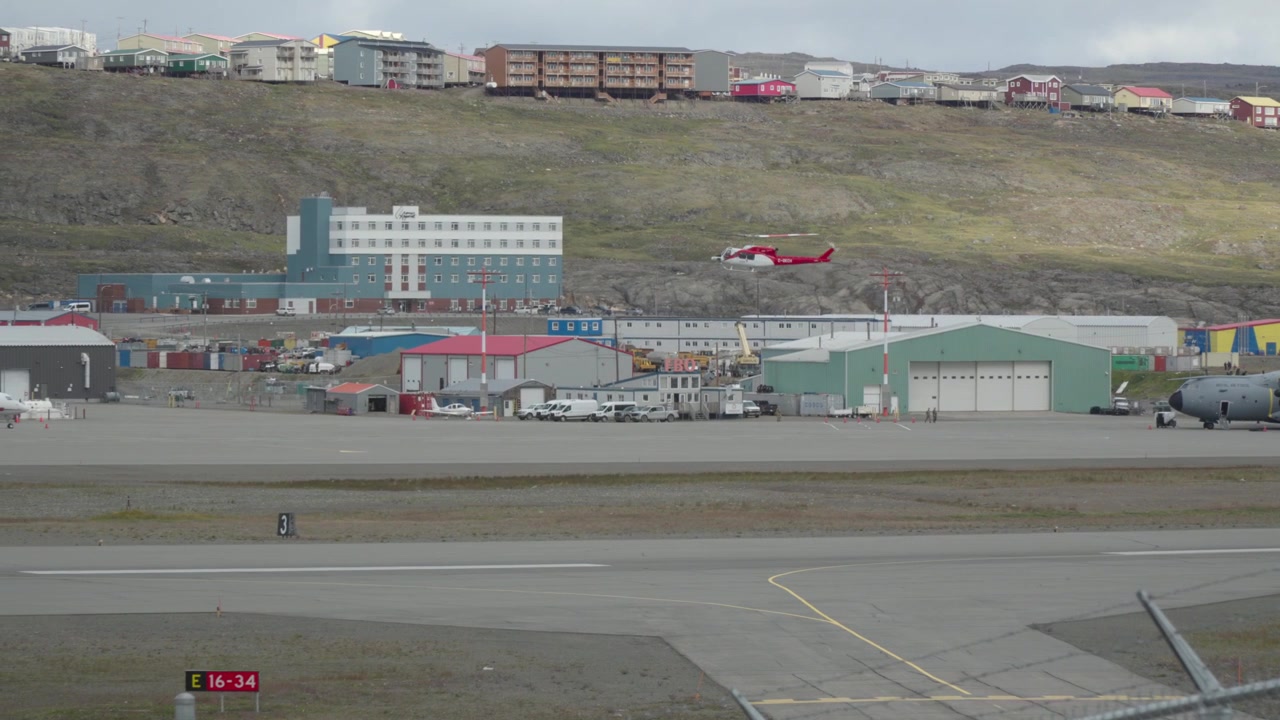 Medium telefotobilde som sporer et rødt helikopter idet det lander på rullebanen og fullfører landingssekvensen på Iqaluit lufthavn.