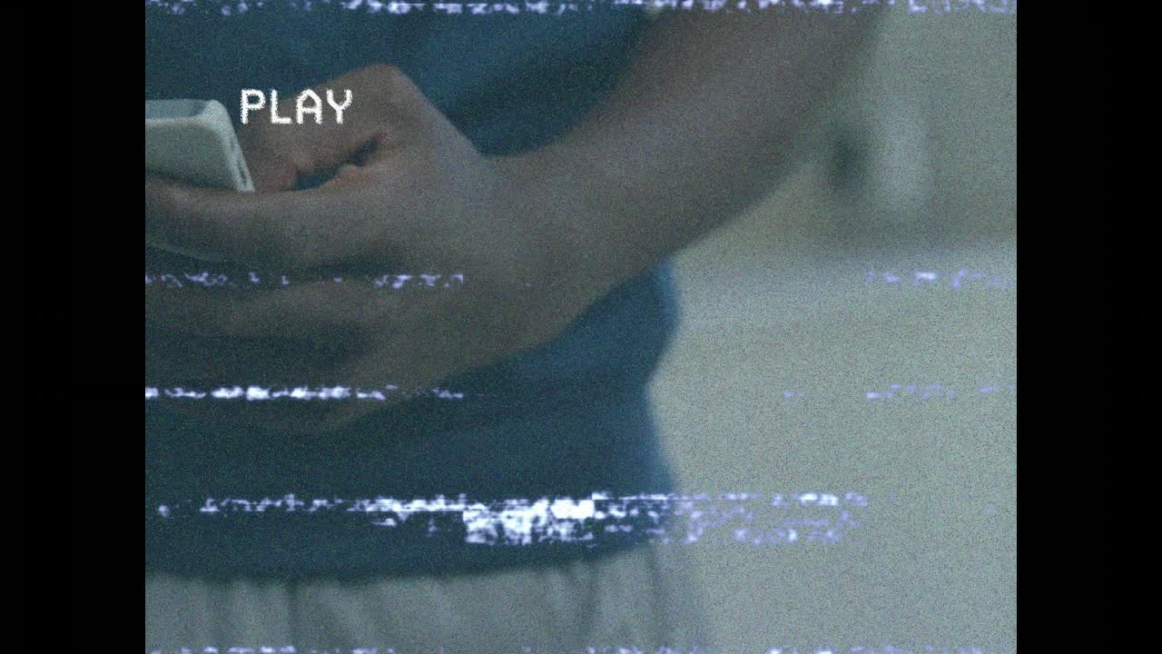 VHSストリーミングの砂嵐が流れる中、モバイルテクノロジーユーザーが友人から水筒を受け取り水分補給をする