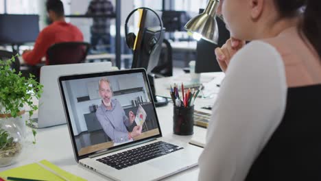 Caucasian-woman-having-a-video-call-on-laptop-with-male-colleague-at-office