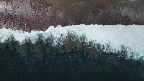 bird's eye view of ocean waves crashing against shore in loyalty islands, new caledonia