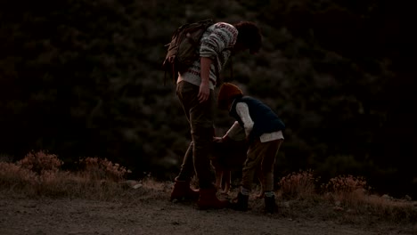 young father and son hikers petting dog on mountain peak