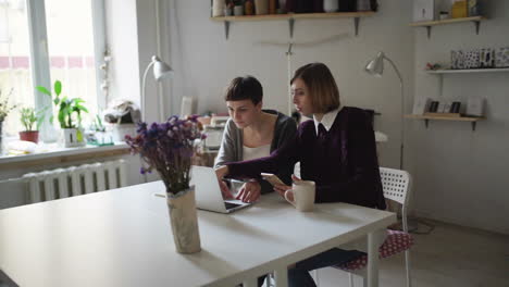 Dos-Mujeres-Creativas-En-La-Mesa-Y-Usando-Un-Cuaderno-Para-Comprar-En-Línea