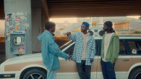 compañía de amigos negros charlando en coche al atardecer bajo un paso elevado urbano