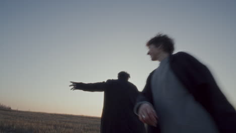 carefree couple spinning together in field during sunset