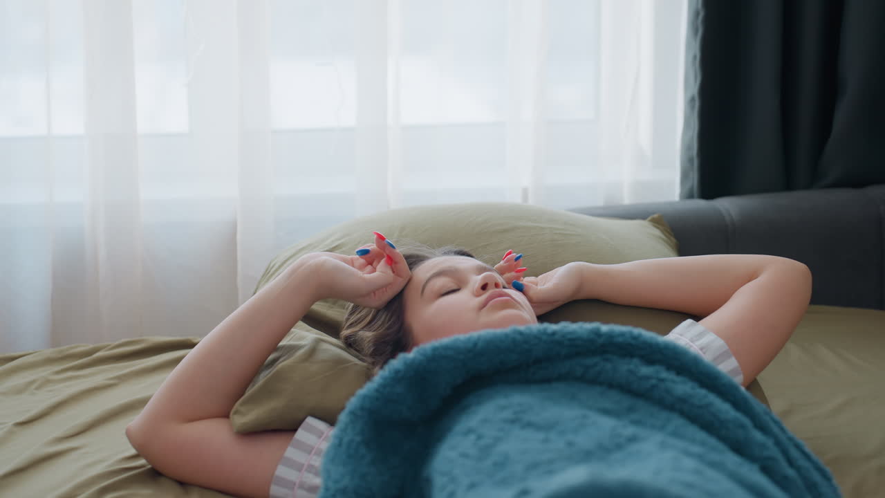 Young Woman Lying On Bed Drowsy, Reaching For Phone And Stretching Adjusting Hair And Rubbing Neck While Staring Toward Window, Soft Blanket And Pillow, Muted Daylight And Sheer Curtains, Pensive