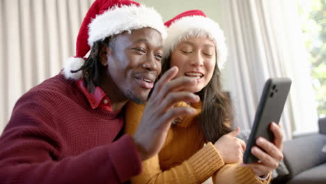 happy diverse couple having christmas video call on smartphone, waving at home, slow motion