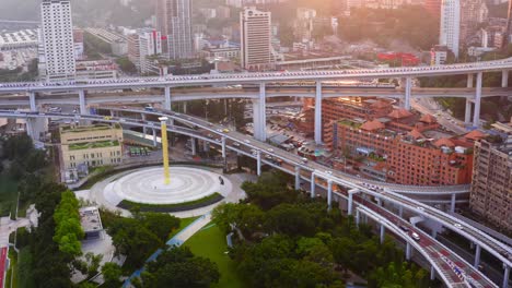 Aerial-orbit-around-bustling-highway-interchange-and-yellow-tower-monument-at-sunset-Chongqing-city-china