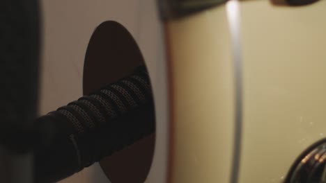 close up of a dynamic large diaphargm microphone placed in a hole of a bass drum, while the drum head is vibrating through playing