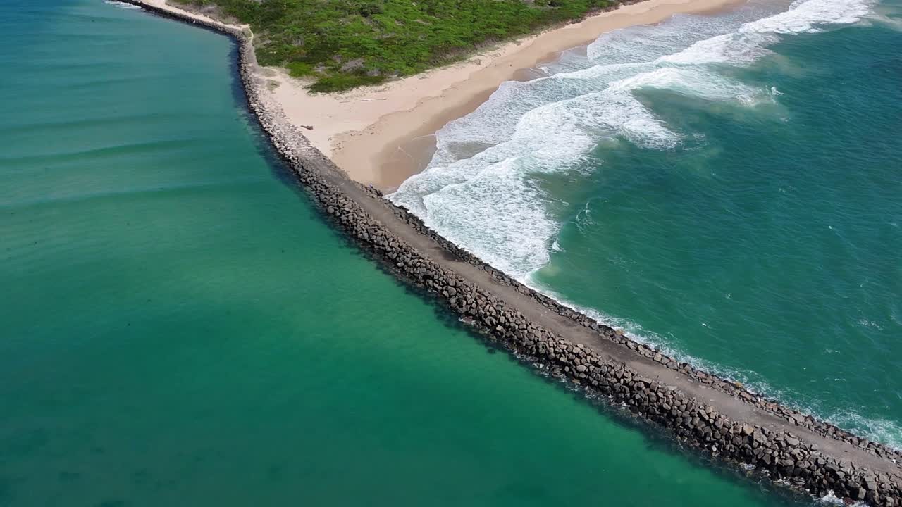 Drone orbit along long breakwater at Windang Passage as waves roll in from the sea on sandy shores
