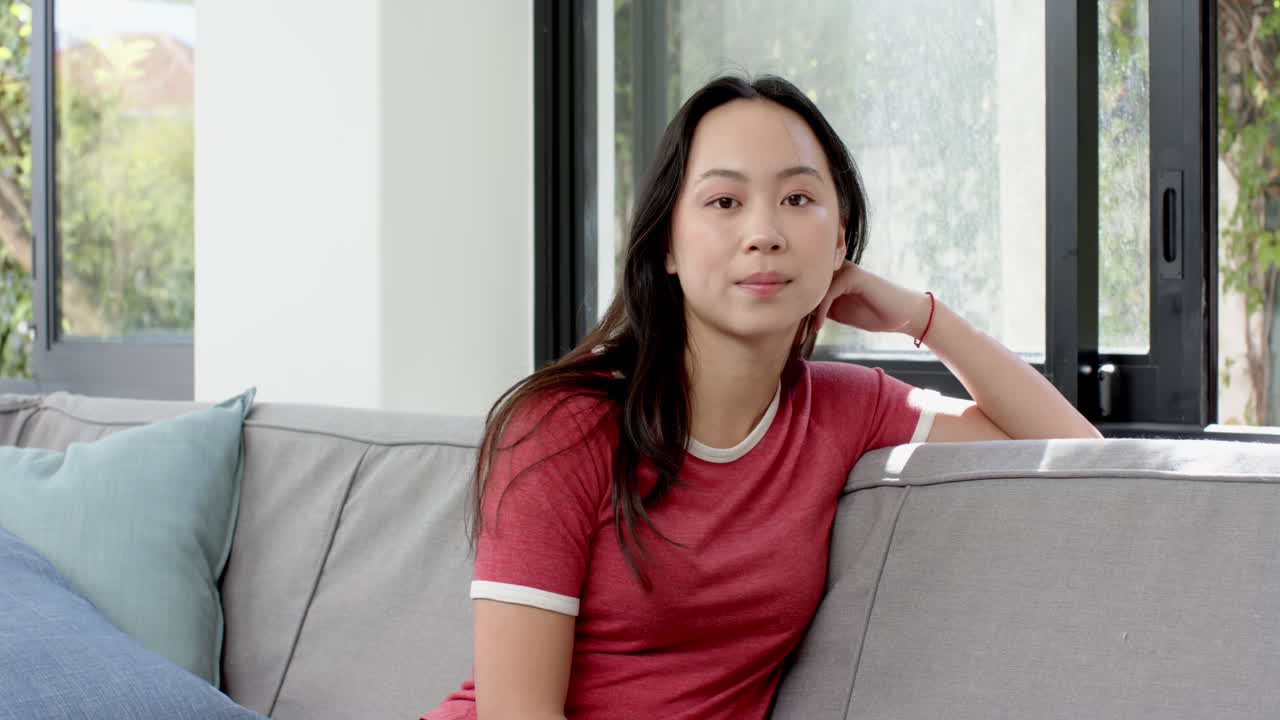 Relaxing on couch, young woman in red shirt smiling at camera